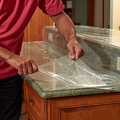 A clear surface protection film is being peeled from a granite countertop.